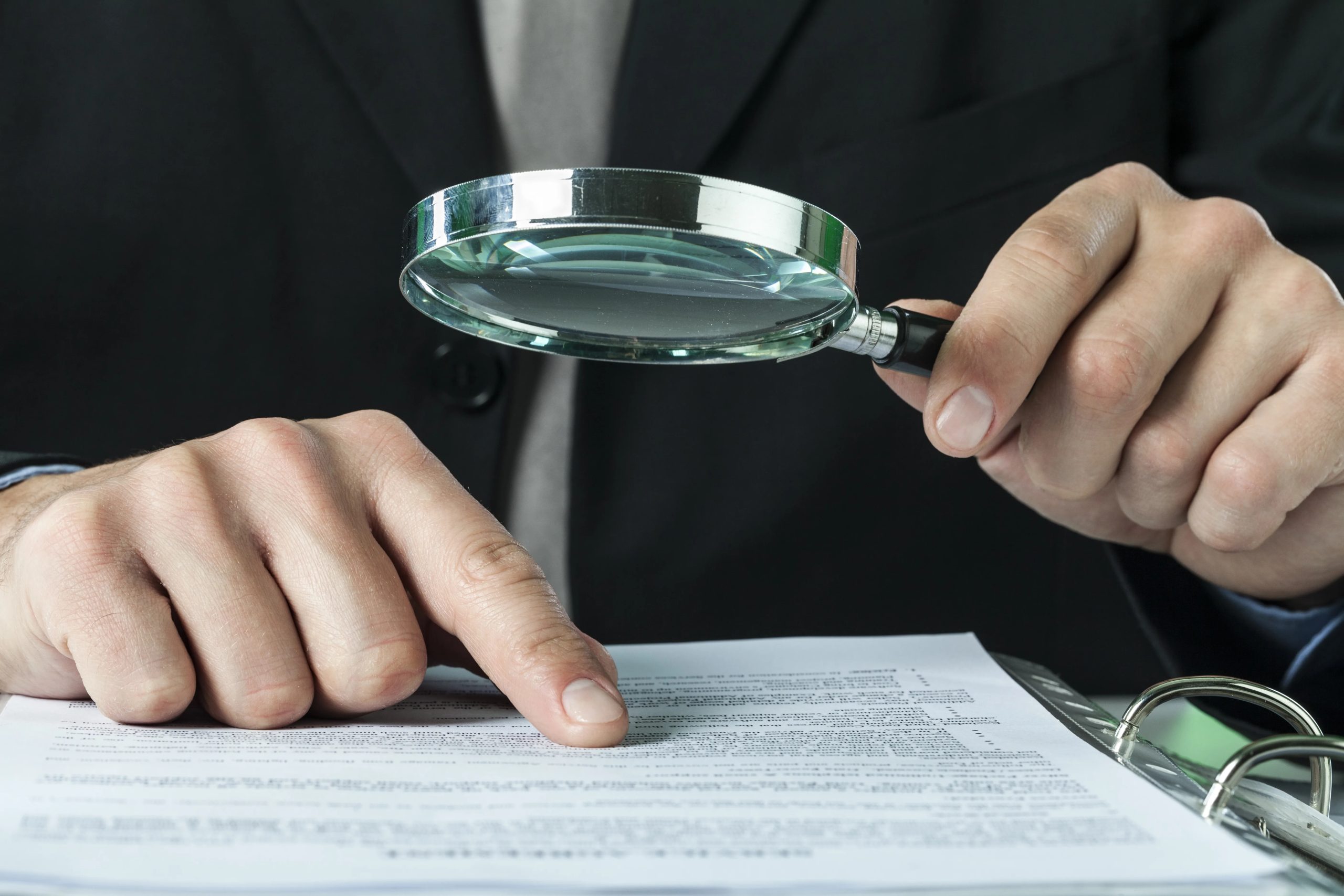 Man reviewing documents closely with a magnifying glass